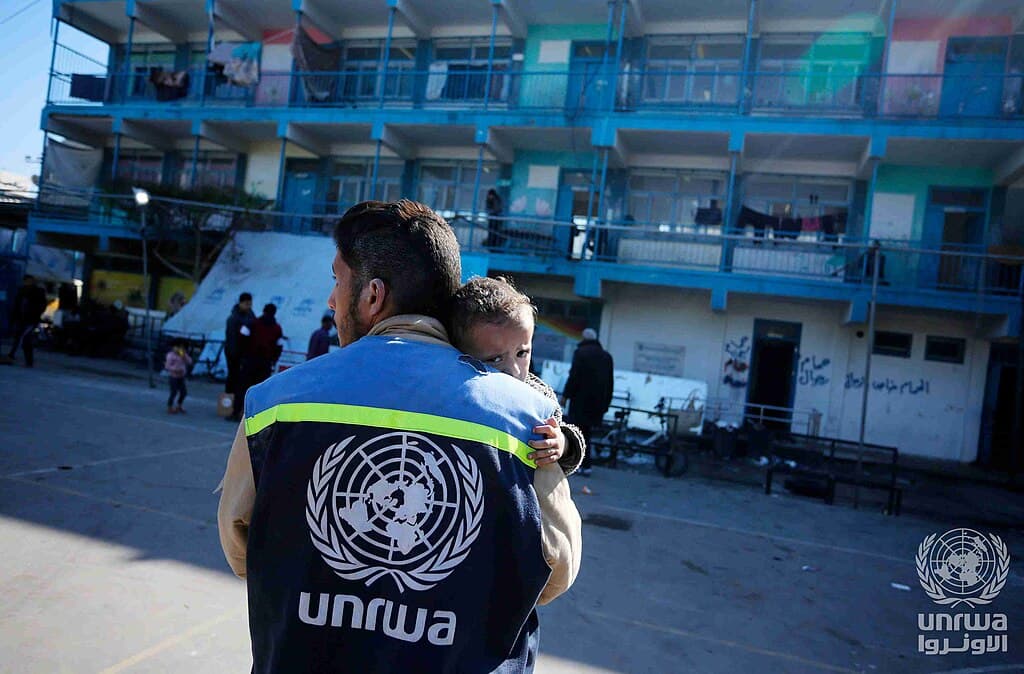 An UNRWA staff member comforts a child at a school shelter in Nuseirat camp, Gaza